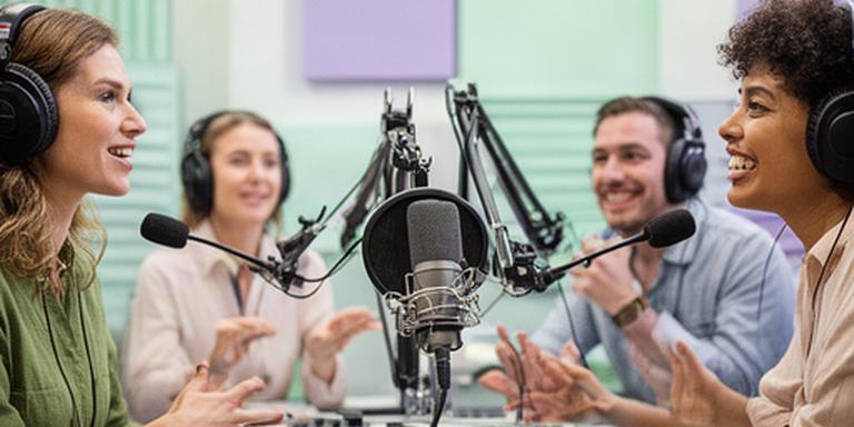 Diverse collega's in een lichte studio met koptelefoons rond een podcastmicrofoon